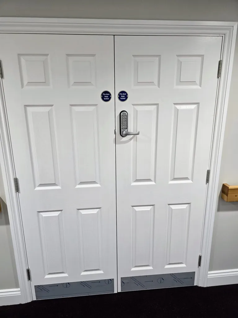 White double doors with raised panels, metal kick plates and central handle in corridor