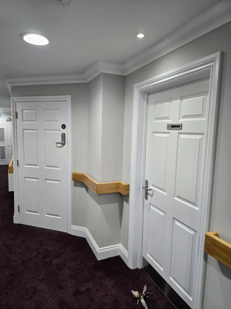 Corridor with multiple white panel doors and wooden handrails along walls