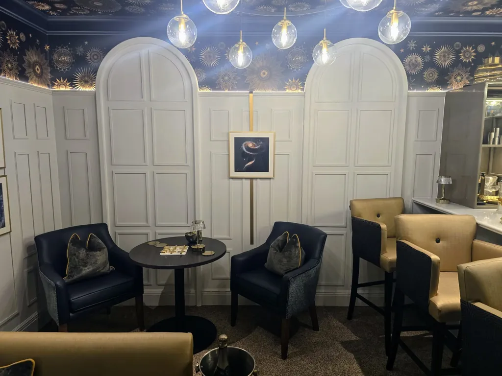 Lounge area with upholstered chairs, round table and decorative wall panelling with lighting