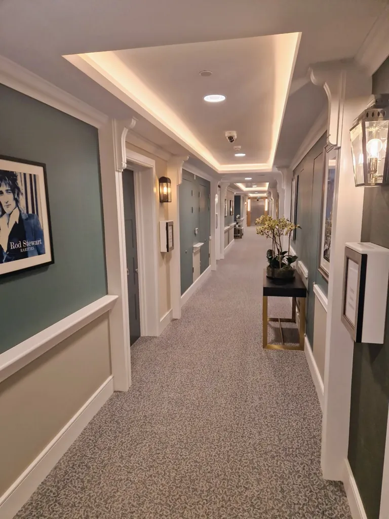 Care home corridor with carpet flooring, wall lighting and decorative furniture