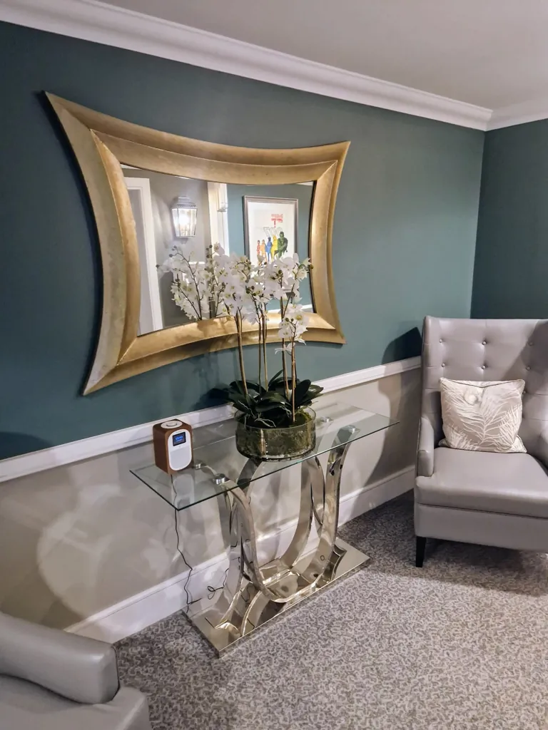 Console table with glass top, decorative mirror and floral arrangement in seating area