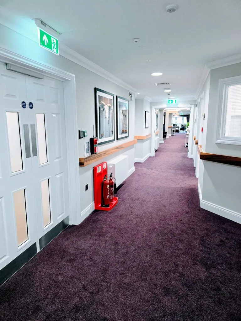 Care home corridor with white fire doors, wall handrails, fire extinguisher and exit signage