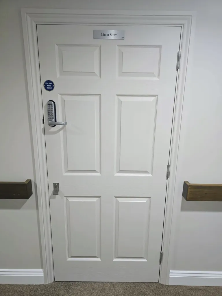White panel door with keypad lock and signage in corridor with wall protection rails
