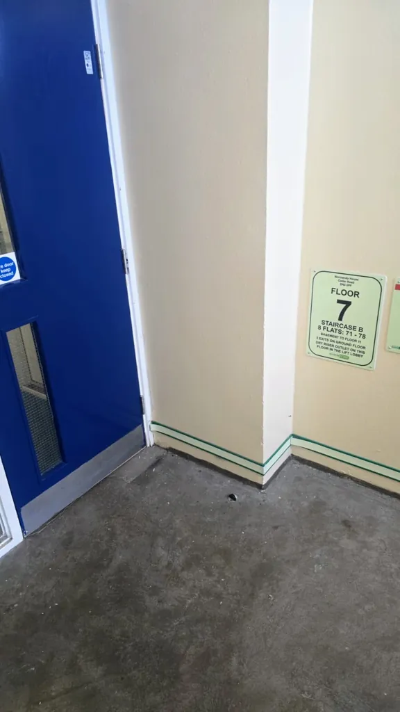 Blue fire door in corridor corner with floor sign and wall-mounted fire door keep shut notice