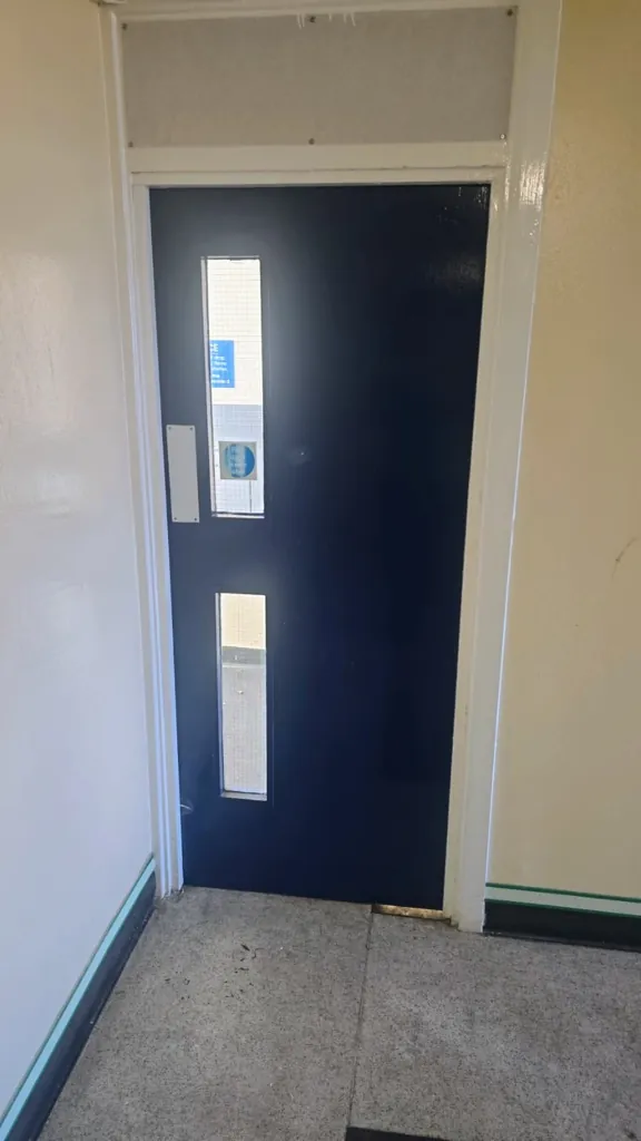 Blue fire door with narrow vision panel and access control keypad in corridor