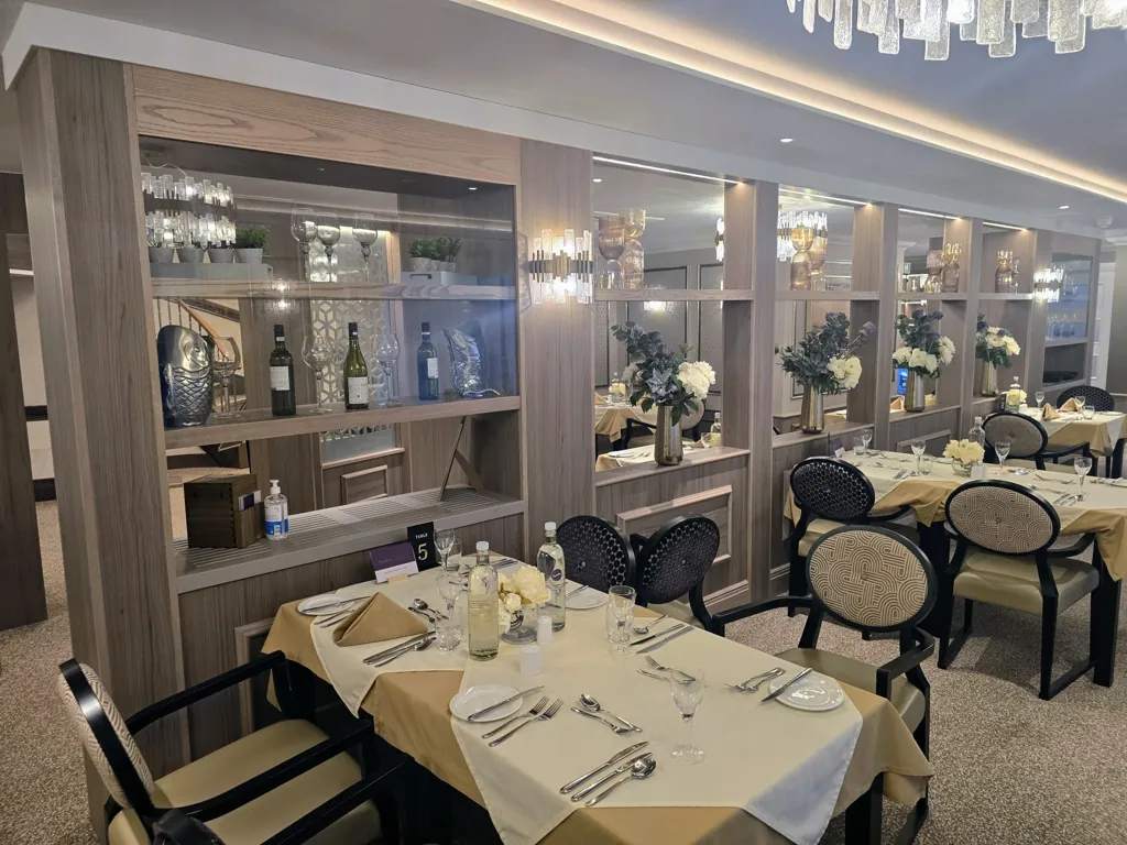 Dining area with set tables, upholstered chairs and decorative shelving with mirrors and lighting