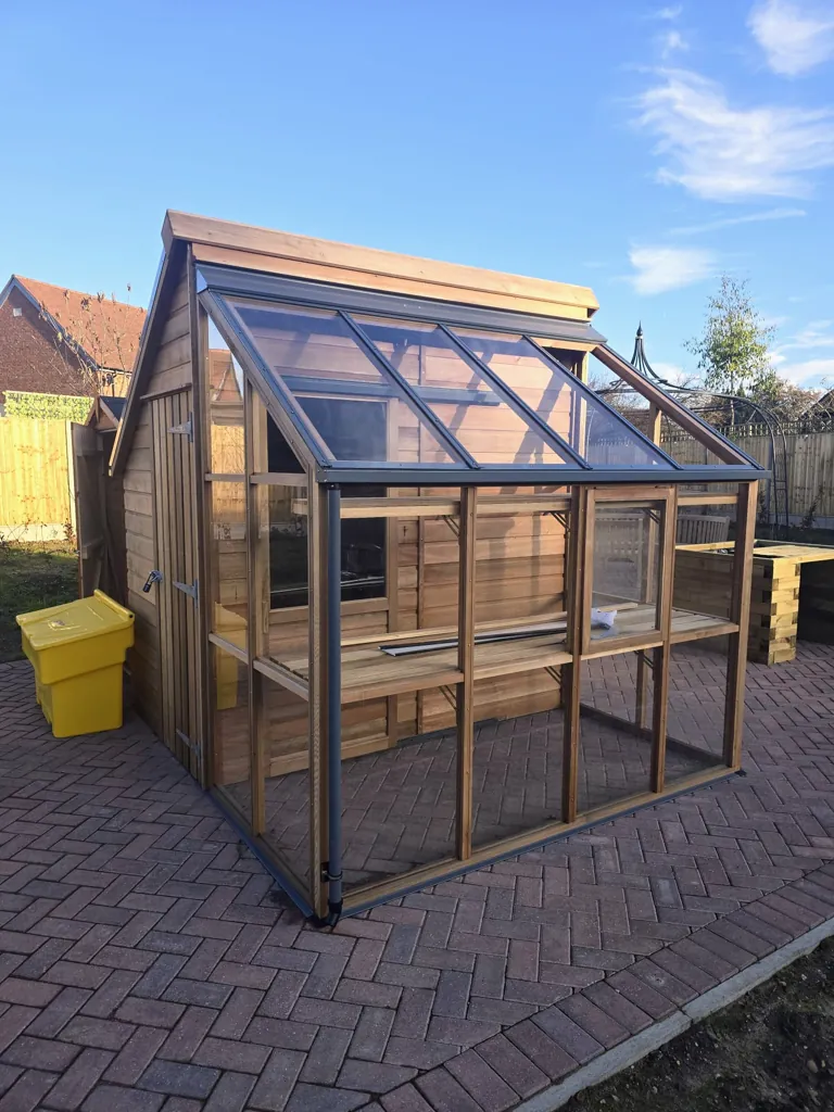 Timber greenhouse structure with glazed panels and wooden frame on paved area