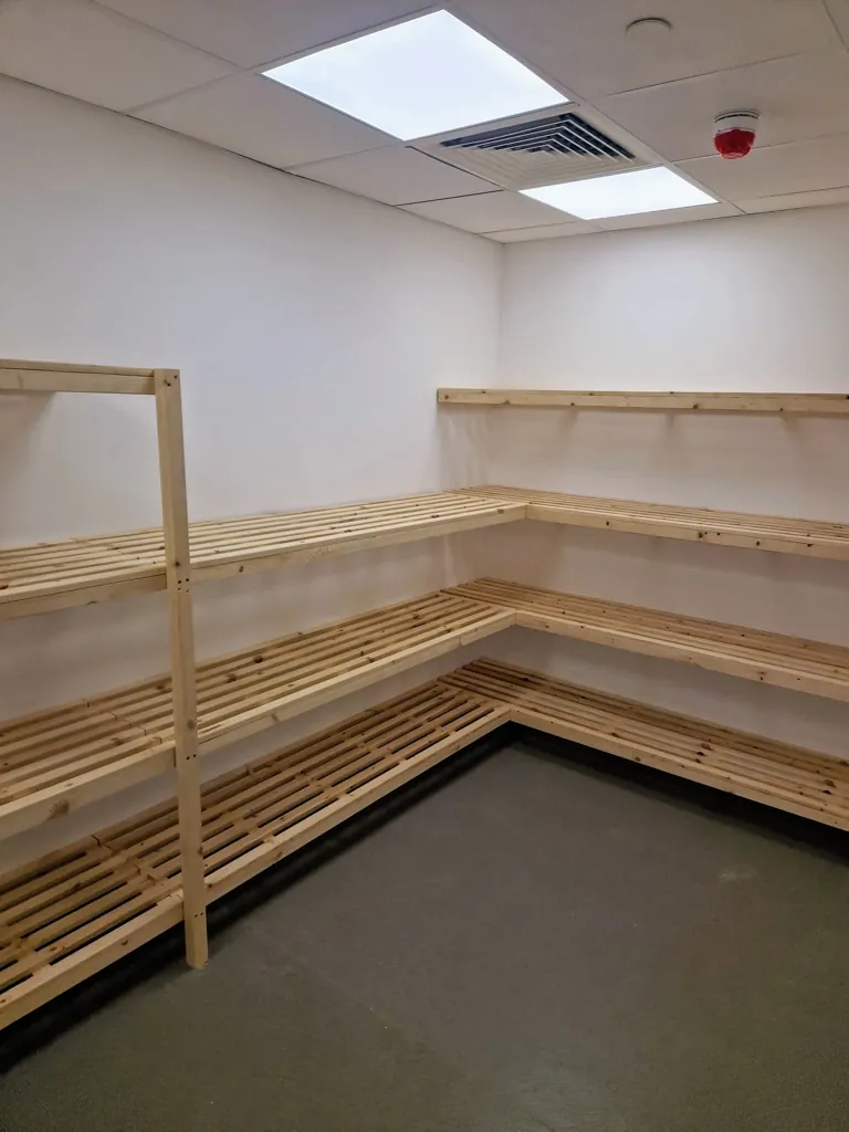 Corner installation of wooden slatted shelves fixed to walls in utility storage space