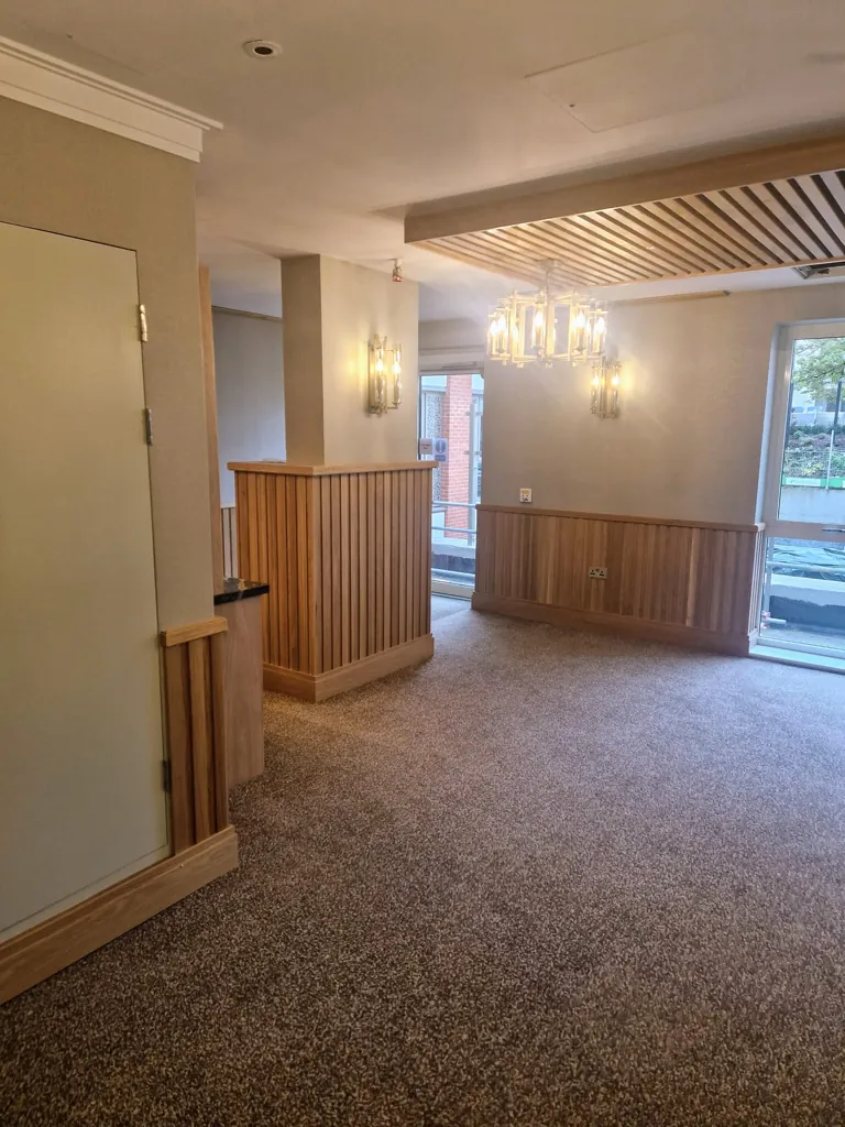 Open interior space with carpet flooring, timber wall panelling and ceiling lighting feature