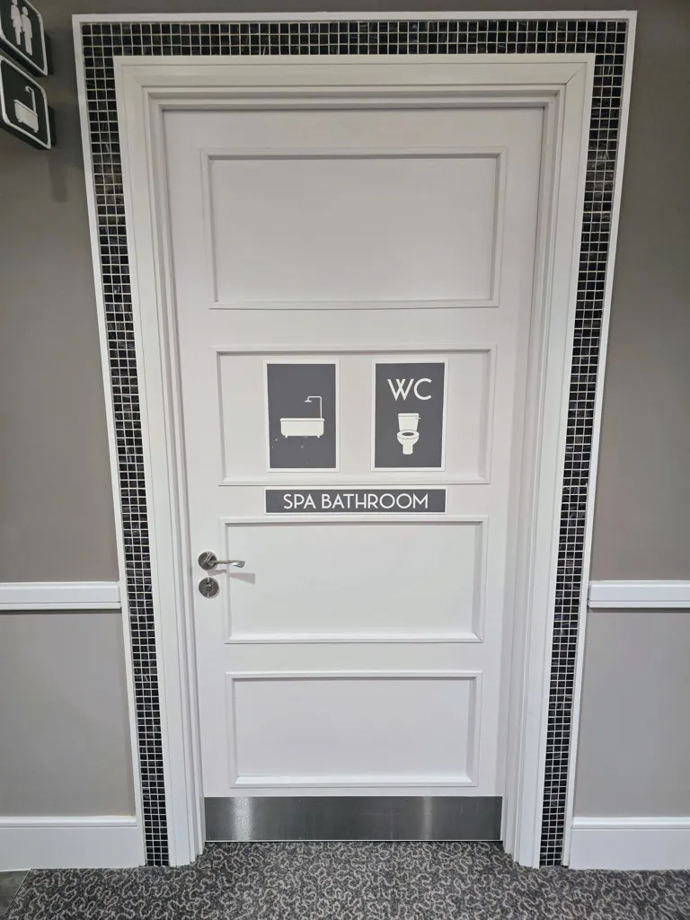 White door with spa bathroom signage and tiled surround in interior corridor